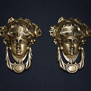 Puede incluir: Un par de aldabas de puerta de latón antiguo con un diseño de rostro de mujer. Las aldabas tienen un diseño detallado con un anillo para golpear.