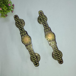 Puede incluir: Dos tiradores de puerta de latón antiguo con un diseño floral. Los tiradores son de color marrón oscuro con detalles en verde y dorado.