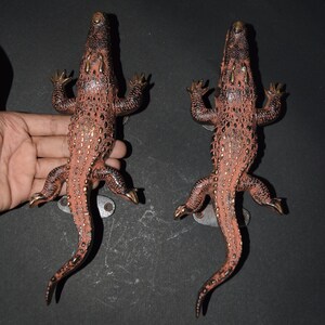 May include: Two bronze-colored alligator door handles. The handles are detailed with a reddish-brown body, dark brown accents, and gold-colored claws. Each handle has a mounting plate for installation.