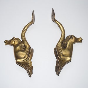May include: A pair of gold-toned metal decorative brackets shaped like a mythical creature with wings and a horse head.
