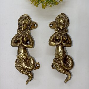 Peut inclure: Une paire de poignées de porte en laiton ornées représentant une figure féminine avec les mains jointes en prière, son corps inférieur est un serpent. Les poignées sont de conception indienne traditionnelle.