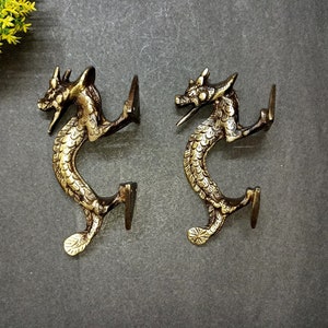 May include: A pair of gold-toned metal dragon door handles. The handles are in the shape of a dragon with its tail curled around to form a handle. The dragons are facing opposite directions.