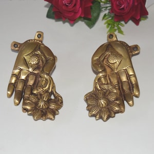 Könnte beinhalten: Zwei goldfarbene, handförmige Wanddekorationen aus Metall mit Blumendesign. Jede Hand hält eine stilisierte Blume mit filigranen Details.