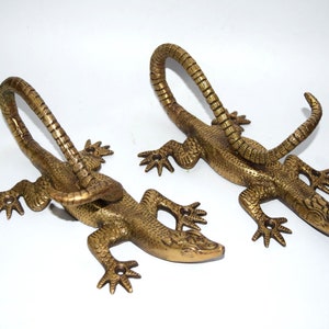May include: Two gold-colored metal lizard wall hooks. The lizards are curled in a decorative pose with their tails forming a hook.