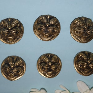 May include: Six gold-coloured metal buttons with a detailed design of a lion's face. The buttons are round and have a raised design.