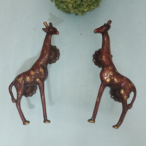 May include: Two gold-toned giraffe door handles with a brown and gold spotted pattern. The handles are in a standing position with their necks arched.