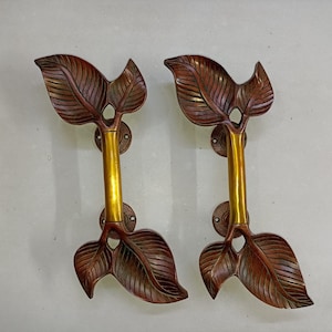 May include: Two ornate door handles with a leaf design. The handles are made of brass and have a gold finish. The leaves are a dark brown color.