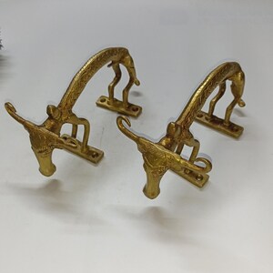 May include: Two gold-toned metal door handles shaped like stylised animals with curved necks and detailed bodies.