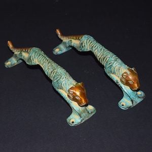 Peut inclure: Une paire de poignées de porte en laiton antique en forme de tigres. Les poignées sont de couleur bleu sarcelle avec des accents dorés.