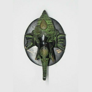 May include: A green and black metal wall hanging of the Hindu deity Ganesha. The elephant head is detailed with intricate carvings and a gold crown.