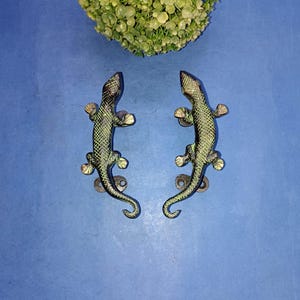 Könnte beinhalten: Zwei antike bronzene Türklinken in Form von Eidechsen. Die Griffe sind mit strukturierten Schuppen verziert und haben eine grüne Patina.