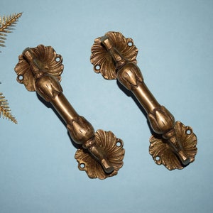 May include: Two ornate brass door handles with a floral design. The handles are a light gold colour and have a detailed, intricate design.