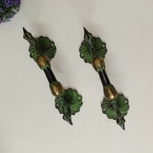 Op de afbeelding: Twee sierlijke messing deurgrepen met een pauwenmotief. De grepen zijn groen en goudkleurig met een zwarte afwerking.