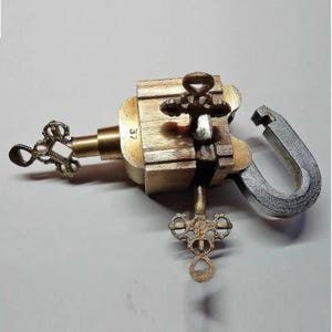 Può includere: Un lucchetto vintage in ottone con corpo in legno e grillo color argento. Il lucchetto presenta fori per chiavi ornati ed elementi decorativi a forma di chiave. Il numero "37" è visibile sul componente in ottone.