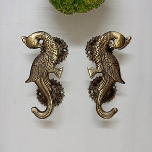 Puede incluir: Dos tiradores de puerta de latón adornados con forma de caballitos de mar estilizados con detalles intrincados. Los tiradores son de color dorado y tienen un diseño floral decorativo.