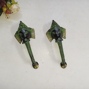 May include: Two decorative brass door handles featuring an elephant head design. The handles are painted in black and green, with intricate detailing on the elephant's face and trunk. The handles are approximately 6 inches long.