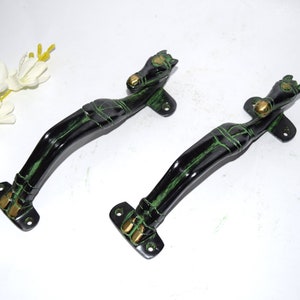 May include: Two black and green door handles with a horse head design. The handles are made of metal and have a curved shape. The horse heads are at the top of the handles, and the handles have a brass accent.