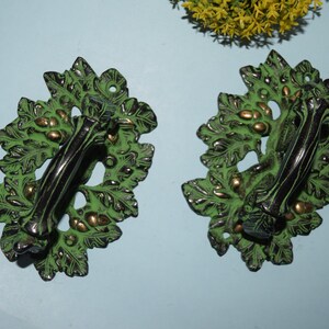 May include: Two green and gold metal door handles with a leaf design. The handles are black and have a leaf design.