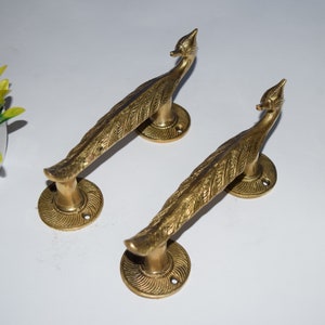 Puede incluir: Dos tiradores de puerta de pavo real dorados con diseños detallados de plumas. Los tiradores están hechos de latón macizo y tienen un estilo indio tradicional.