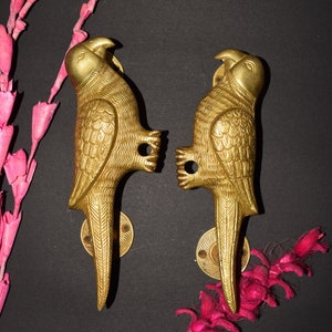 Könnte beinhalten: Zwei goldfarbene Metall-Parrotentürgriffe. Die Griffe sind mit aufwendigen Schnitzereien verziert und haben eine runde Basis.