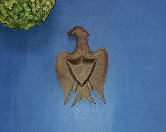 May include: A bronze eagle sculpture with its wings spread wide. The eagle is standing on a small base and has a detailed design.