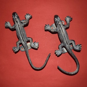 May include: Two black metal lizard door knockers with detailed scales and curled tails.