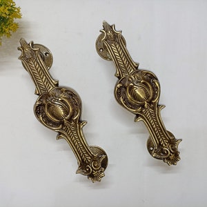 May include: Two ornate brass door handles with intricate floral designs. The handles are a traditional style with a decorative finish.