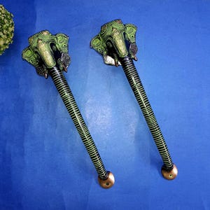 May include: Two decorative door handles with an elephant head design in green and black. The handles have a long, ribbed shaft with a brass-colored base. The elephant heads are intricately detailed with green patterns.