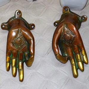 May include: Two ornate brass hand-shaped door handles with a green and gold finish. The hands are in a gesture of giving or receiving.