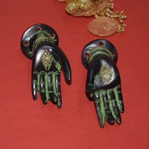 Può includere: Due maniglie per porte in metallo nero a forma di mano con dettagli dipinti in verde e accenti dorati. Le maniglie hanno un design a forma di diamante al centro del palmo.