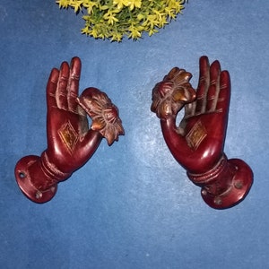 May include: A pair of ornate red metal door handles with a flower design. The handles are in the shape of hands with the fingers curled inwards.