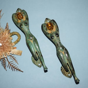 May include: Two decorative door handles in the shape of a woman, with a green patina finish and gold accents.