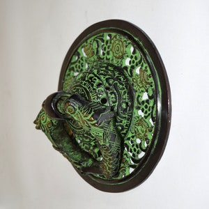 May include: A green and black metal door knocker with a decorative design. The knocker is shaped like two fish with their tails intertwined.