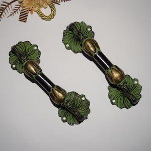 May include: Two ornate green and gold door handles with a black metal bar. The handles are shaped like stylized leaves and flowers.