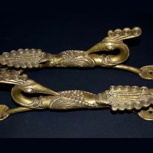 Puede incluir: Un par de tenazas de servir de metal dorado adornadas con forma de pavo real. Las tenazas tienen un diseño detallado con patrones intrincados y un extremo en forma de tenedor.