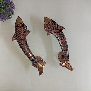 Può includere: Due maniglie per porte decorative a forma di pesce in ottone con finitura marrone e dorata.