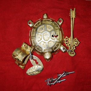 May include: A brass turtle-shaped lock mechanism featuring a decorative shell with a keyhole, a matching ornate skeleton key, a separate brass mounting bracket with a small oval plate, and a collection of silver-colored metal screws and nuts.