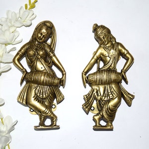 May include: Two gold-toned metal sculptures of people playing traditional Indian instruments. The sculptures are detailed and have a realistic appearance.
