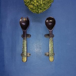 Puede incluir: Un par de tiradores de puerta de metal negro con detalles en verde y dorado. Los tiradores tienen forma de cucharas y tenedores.