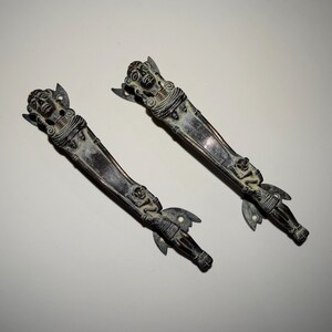 May include: Two antique bronze door handles with ornate designs featuring human figures. The handles have a dark patina and are in good condition.