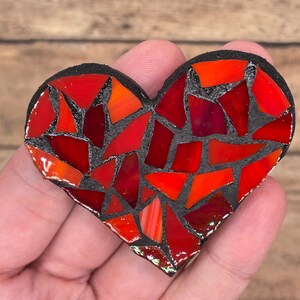 May include: A red and black mosaic heart with a black grout. The heart is made of small, irregular pieces of glass.