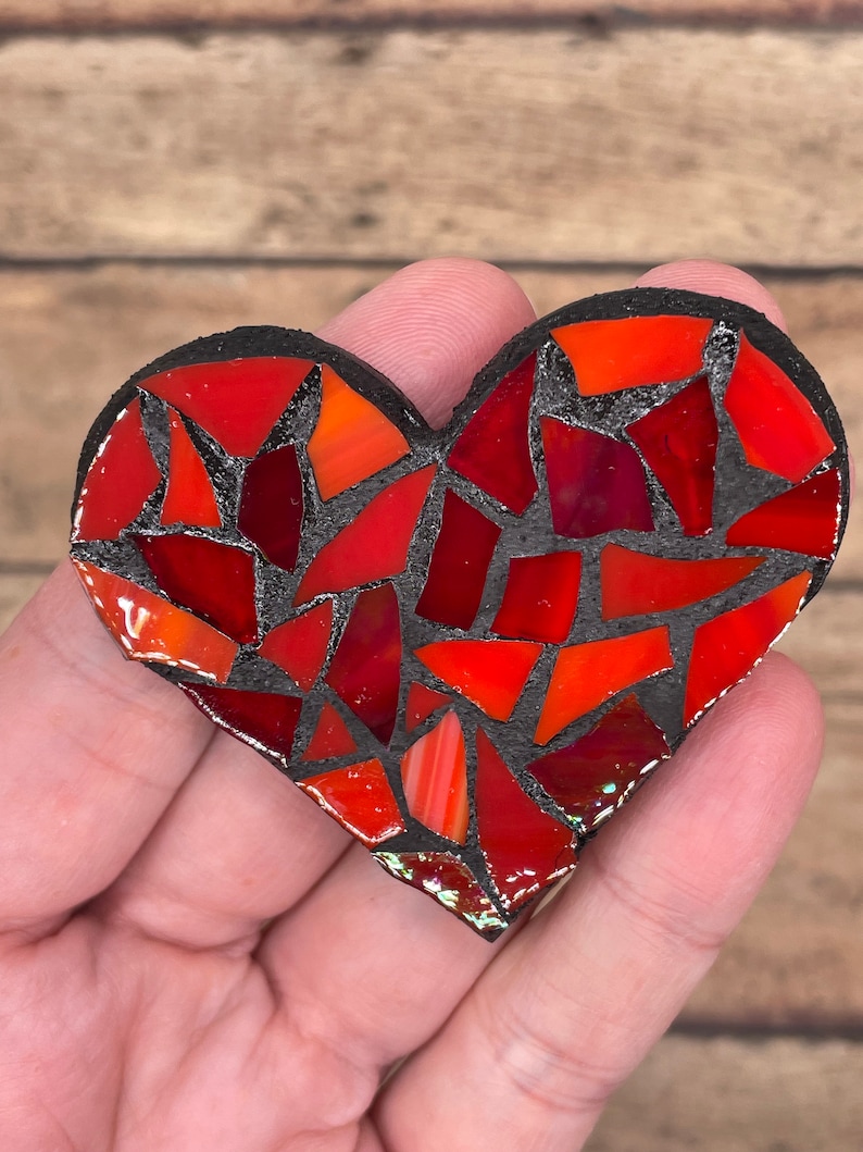 May include: A red and black mosaic heart with a black grout. The heart is made of small, irregular pieces of glass.