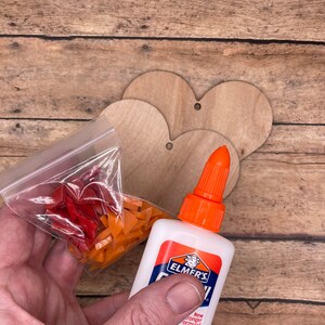 May include: A close-up of a bottle of Elmer's glue with a new stronger formula. The bottle is white with orange and red accents. A bag of orange and red mosaic tiles is in the background.