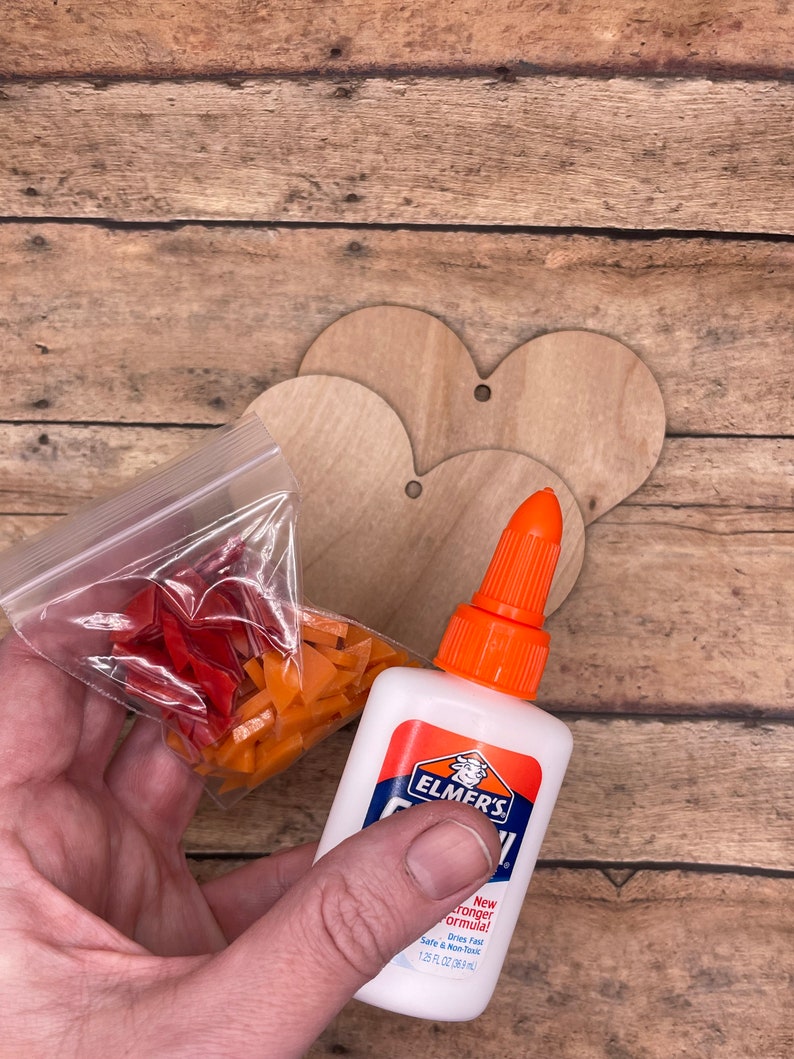 May include: A close-up of a bottle of Elmer's glue with a new stronger formula. The bottle is white with orange and red accents. A bag of orange and red mosaic tiles is in the background.