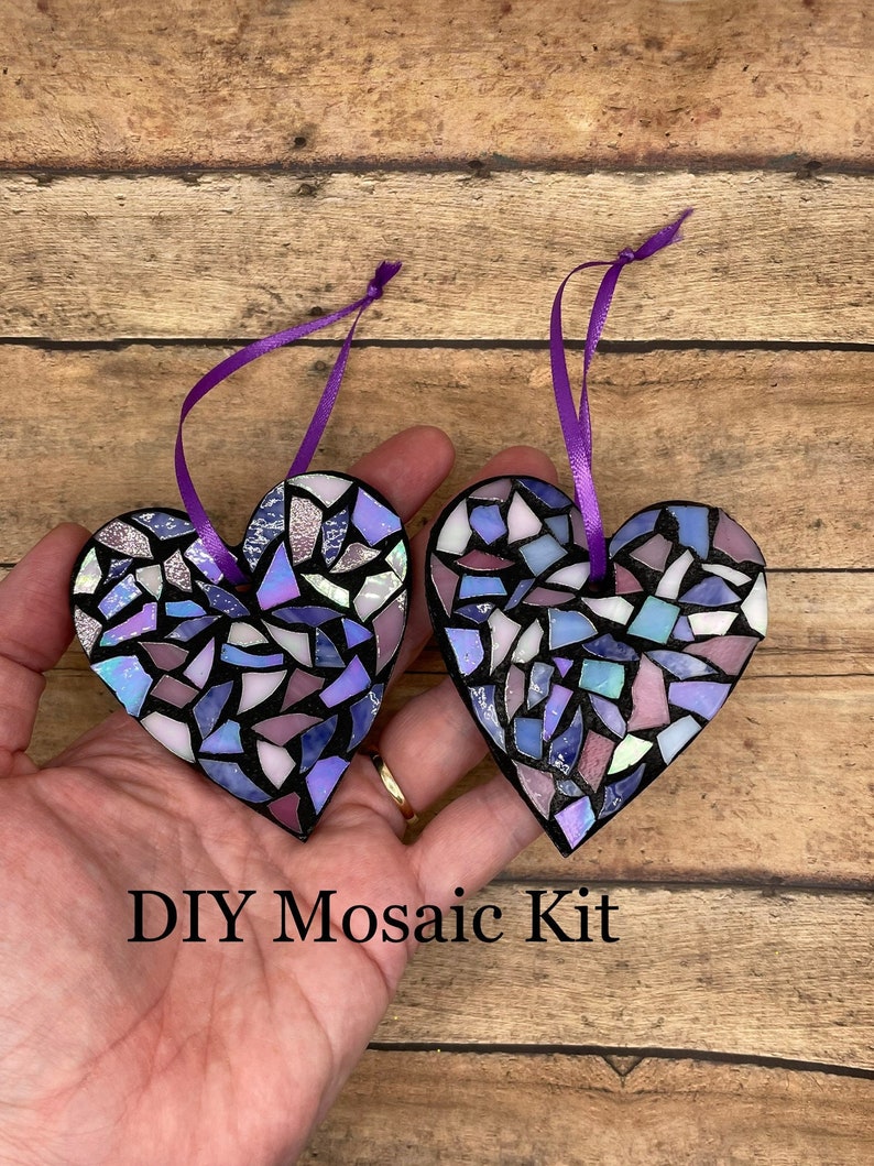 May include: Two purple and blue mosaic heart ornaments with a black outline and a purple ribbon attached to each. The text "DIY Mosaic Kit" is visible in the image.