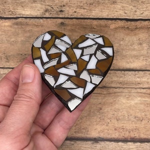 May include: A heart-shaped mosaic made of brown, white, and silver glass tiles. The mosaic is handmade and has a rustic, vintage look.