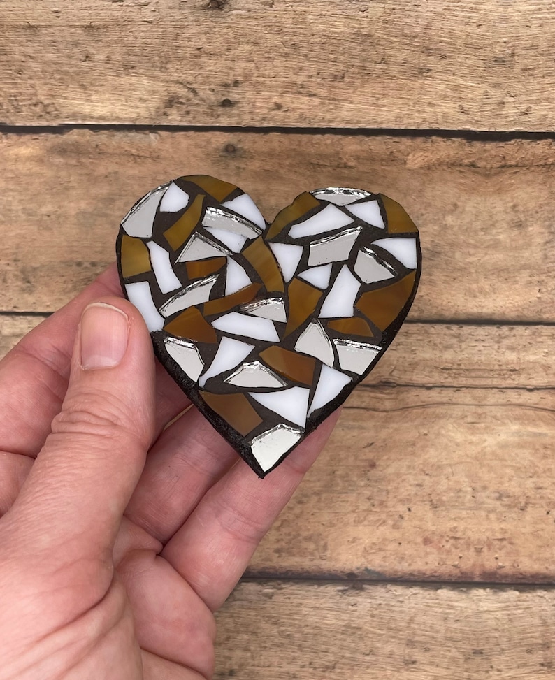 May include: A heart-shaped mosaic made of brown, white, and silver glass tiles. The mosaic is handmade and has a rustic, vintage look.