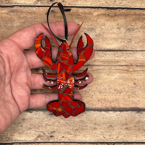 Może przedstawiać: Ozdoba w kształcie homara wykonana z czerwonej i pomarańczowej mozaiki z czarnymi oczami i czarną sznurkiem do zawieszenia.