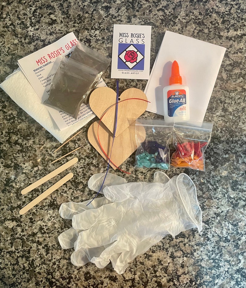 May include: A glass art kit with two wooden heart-shaped ornaments, glass pieces in blue, green, and orange, glue, and a pair of gloves. The kit also includes instructions and a small bag of glass glitter.