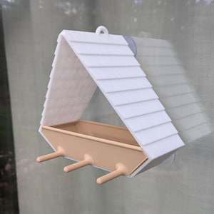 Peut inclure: Un mangeoire à oiseaux blanc et beige, fixé à une fenêtre. Il présente un toit en pente avec un design à lattes et un plateau d'alimentation avec trois petits perchoirs. Conçu pour attirer les oiseaux.